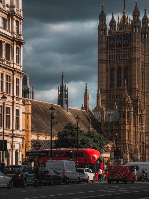 A view of Westminster, London, during daylight hours with the prominent Big Ben clock tower and the Houses of Parliament in the background. The foreground features a busy street with multiple cars par